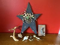 Overview of all decorative items showing wooden star, driftwood bird, wooden block with crab hook, coral, seashell, anchor, and brass hook on wood surface against red wall