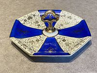 Front view of octagonal porcelain dish with alternating cobalt blue and white panels with gold detailing and gold-tone handle.