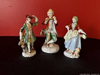 Front view of three Occupied Japan porcelain figurines on red background showing detailed costume and features