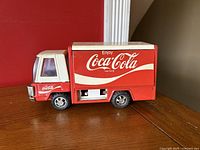 Front and right side view of vintage Coca-Cola Buddy L metal toy truck showing red and white paint, logo on side, and condition.