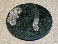 Top view of the round green marble cheese board showing the pewter pine cone decoration and cheese knife placed on the board