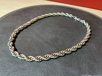 Silver tone twisted rope chain necklace laid on a dark round mat showing the texture and shine of the chain links.