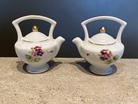 Front view of vintage teapot salt and pepper shakers showing pink rose floral decoration and gold trim accents on white ceramic.