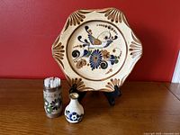 Photo of the large stoneware Tonala plate on stand with the small pottery vase and toothpick holder in front, showing hand-painted floral and bird designs.