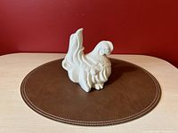 Front view of white ceramic chicken planter on brown placemat with red background