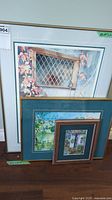 Four framed art prints stacked against a wall, showing size and framing details