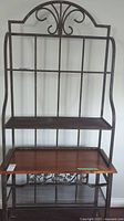 Full view of the baker's rack showing the decorative metal frame, wood shelf, and lower metal shelves.