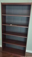Front view of tall brown wooden bookcase with five shelves