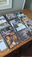 Photo of 20 music CDs arranged on wooden table, featuring artists such as ABBA, Nana Mouskouri, Cher, Elton John, and more