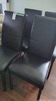 Four black faux leather upholstered dining chairs grouped on a hardwood floor, showing seat and top back view