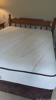 Wooden bed frame with headboard and turned spindles with memory foam mattress and box spring shown from side angle.