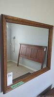 Mirror mounted on wall showing reflection of bed headboard in room corner.