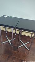 Pair of black lacquered wood top side tables with polished metal legs in X-shaped base design on hardwood floor.