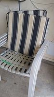 Close-up of one metal patio chair showing white plastic webbing seat and striped cushion with beige, black, and white stripes.