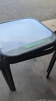Close-up photo showing black framed patio side table with clear glass top, dusty and in need of cleaning.