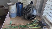 Three pottery vases and decorative green stems with twisted vines placed on a tiled surface near a window.