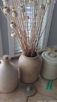 Photo of three pottery pieces beside window: jug, crock, and vase with dried poppy pods