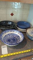Wide view showing a large blue and white speckled bowl, dark swirl bowl, stack of smaller blue bowls, and lidded bowl.