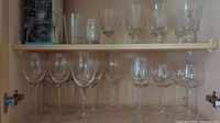 Shelved collection of various sized clear stemware glasses, including large red wine glasses, medium and small stemmed glasses.