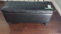 Front and side view of black faux leather storage bench on dark wooden floor