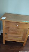 Front view of vintage wooden side table showing drawer and door with white ceramic knobs