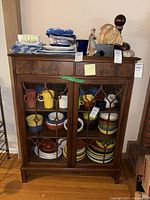 Front view of antique wooden bookcase with glass doors, showing three shelves filled with colorful ceramics and two drawers at top.