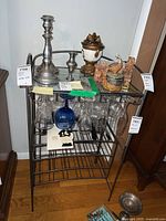 Front view of metal bar rack with top shelf holding various items and lower section designed for holding bottles. Stemware glasses hanging from upper slots.