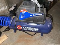 Front and side view of Campbell Hausfeld air compressor showing brand labeling and blue air hose coiled attached.
