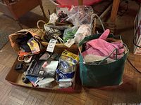 Wide view of assorted household utility items including gardening gloves, cords, and small tools packed in bags and boxes on a floor.