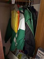 Closet view showing multiple jackets: green Celtics windbreaker, black leather jacket and yellow-packaged garment