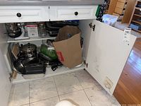 Photo of open cabinet showing variety of pots, pans, and a paper bag with kitchen items inside.