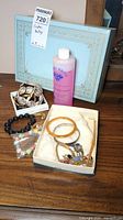 Photo showing multiple bracelets and bangles in boxes on a wooden surface including pink bottle and blue decorative box in background