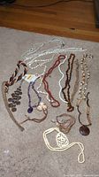 Full view of 9 costume necklaces laid out on carpet, displaying various styles, materials and colors.