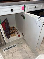 Kitchen lower cabinet open showing two cutlery sets inside, one in a wooden knife block and another colorful unicorn shaped knife holder.