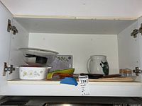 Shelf with Corning Ware baking dish, glass bowls, Arabia Bull pitcher, kitchen shears, cutlery, and canisters arranged inside.