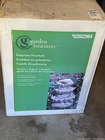 Photo of the front of the original box packaging showing the brand Garden Treasures, the product type (polyresin fountain), model number 0352264, product measurements, and a picture of the fountain.