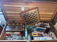 Wide top-down photo of open wooden chest showing multiple board games and items packed inside, including a chess board leaning against the chest top.