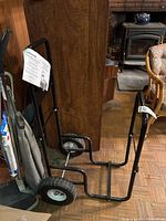 Log caddy angled side view showing tubular black metal frame, base, and one wheel.