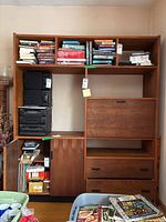 Front view of the Mid-Century Modern teak cabinet with shelving, drop-front door, drawers, and cabinet door. Various media and books stored in the shelves. Note drawers visible and drop-front door closed.