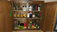 Full view inside vintage wooden cabinet showing assortment of teapot, cups, glasses, bottles, shakers, and small dishes arranged on shelves.
