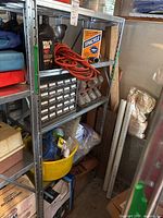 Metal shelving in a garage with assorted fasteners, chemicals, extension cord, spackle, and motor oil visible