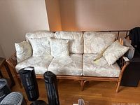 Photo of the rattan framed sofa with three seat cushions, three back cushions, and four throw pillows. Shows the overall condition and floral upholstery pattern.