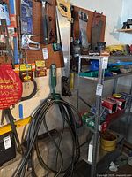Photo showing hand saws on a pegboard, garden and washer hoses coiled on hooks, boxes of staples on shelf, and garden worklight.