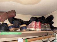 Shelf holding multiple pairs of shoes and boots including Budweiser hi-tops and Timberland boots