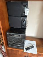 Photo of the assembled Sony stereo system with both speakers on a wooden shelf, showing the main unit, speakers, remote, and manual laid next to it.