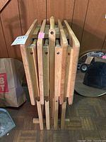 Side view of the five wooden TV tray tables neatly stored in the wooden stand, showing their thickness and handles.