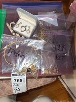Mixed jewelry items in labeled Ziploc bags and a white jewelry box, showing necklaces, brooch, earrings and chain segments.