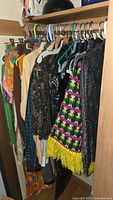 Photo showing assorted hangers with a variety of vintage clothing including colorful and patterned dresses, tops, and jackets hung closely on a closet rod.