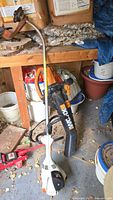Full view showing Worx WG500 blower and Stihl weed trimmer on shed floor with background clutter and rodent droppings.