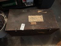 View of closed wooden trunk with worn top surface and metal hinges.